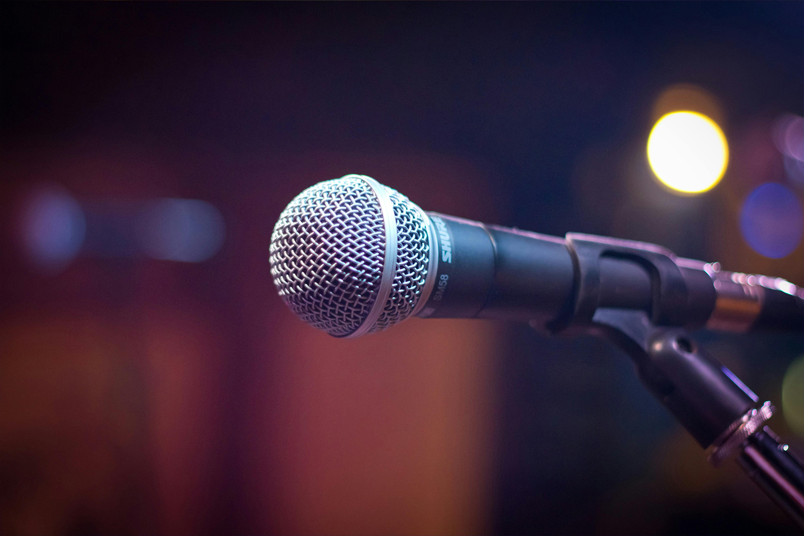 A close up photo of a microphone on a stand with warm colored bokeh in the background