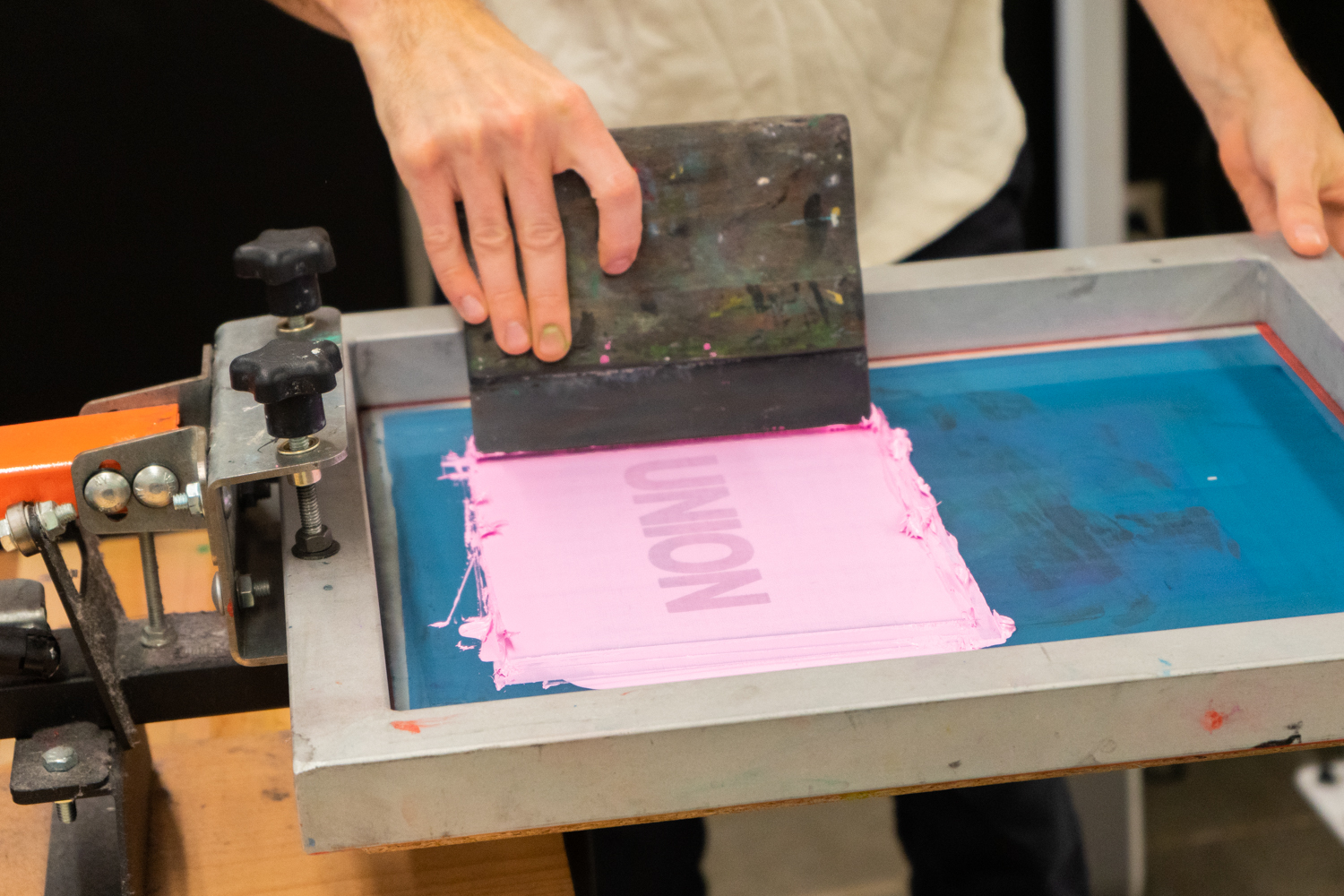 A hand pulls ink across a screen printing screen with a squeegee