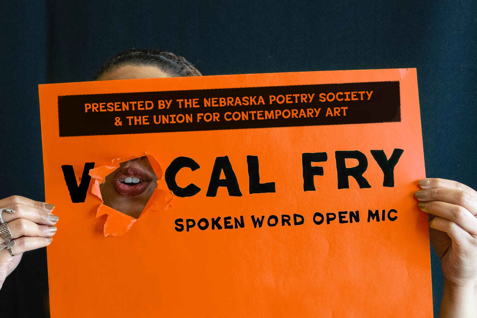 Happenings Vocal Fry 2025 Orange A person holding a paper that says vocal fry there is hole in the paper showing their mouth