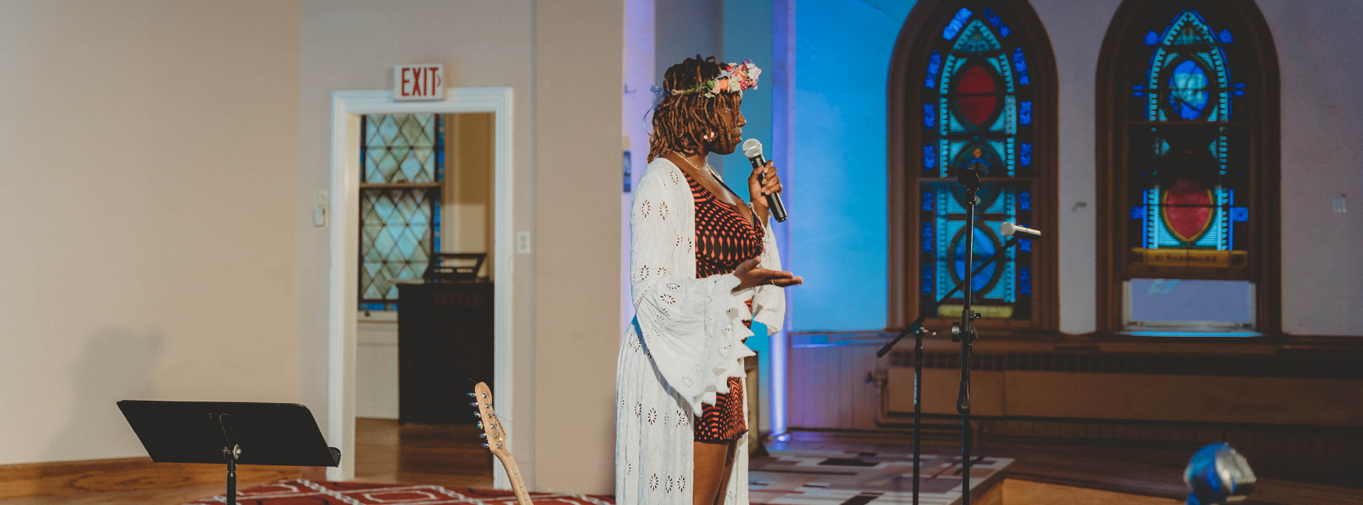 Header Artist Alajia Mc Kizia stands in profile holding a microphone