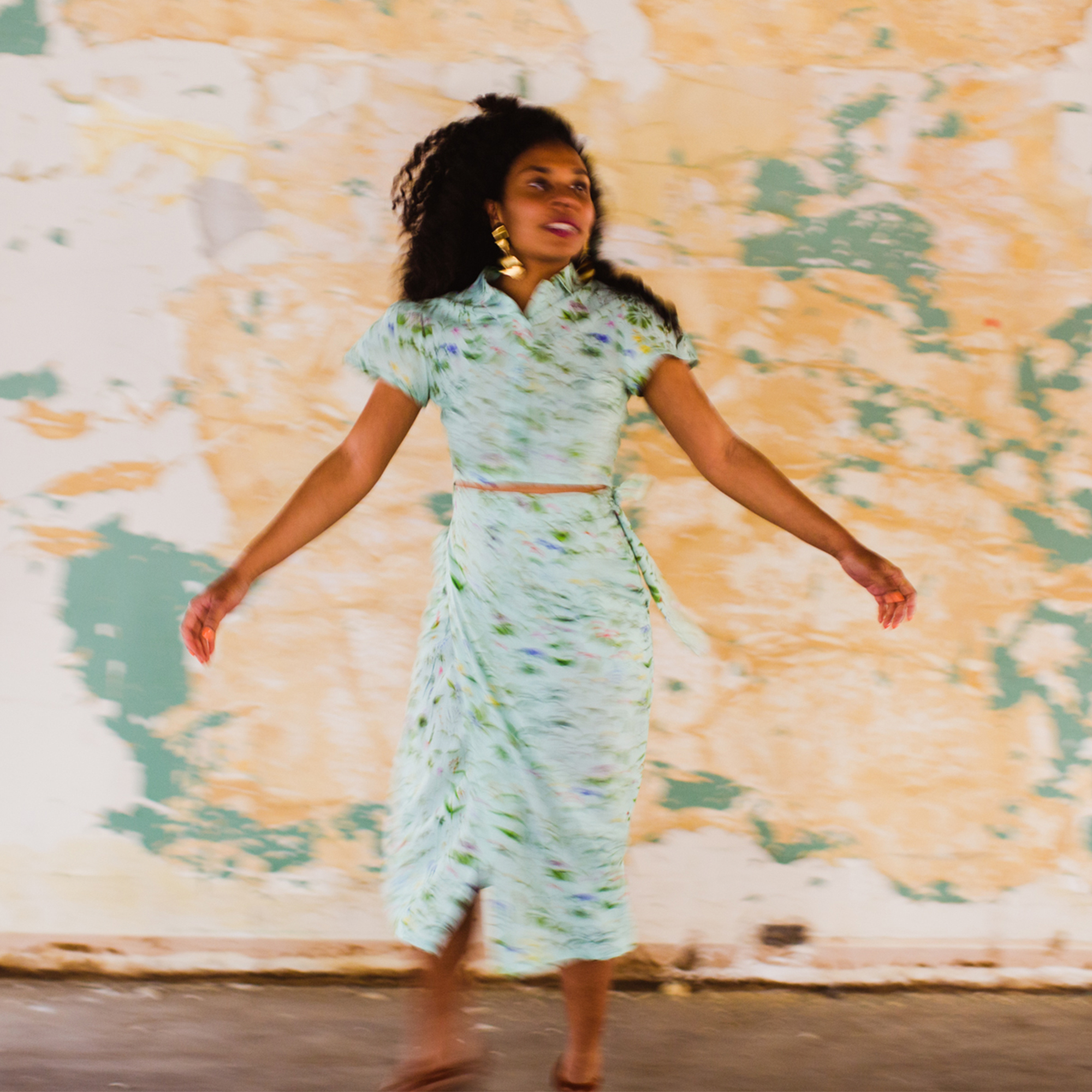 Mary Lawson aka Mesonjixx Stands Arms Streched Out In Front Of A Yellow And Blue Wall Crop