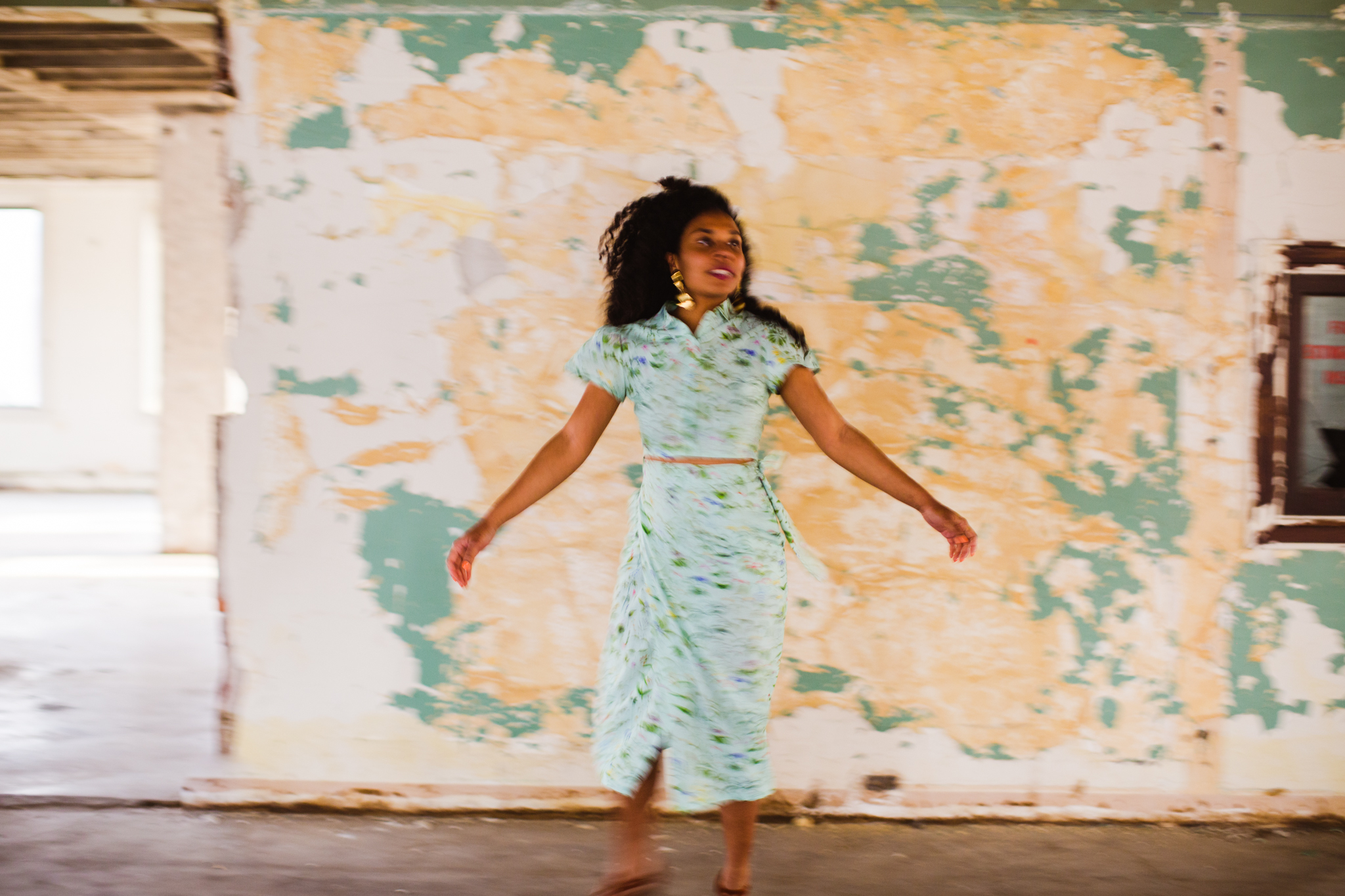 Mary Lawson aka Mesonjixx Stands Arms Streched Out In Front Of A Yellow And Blue Wall