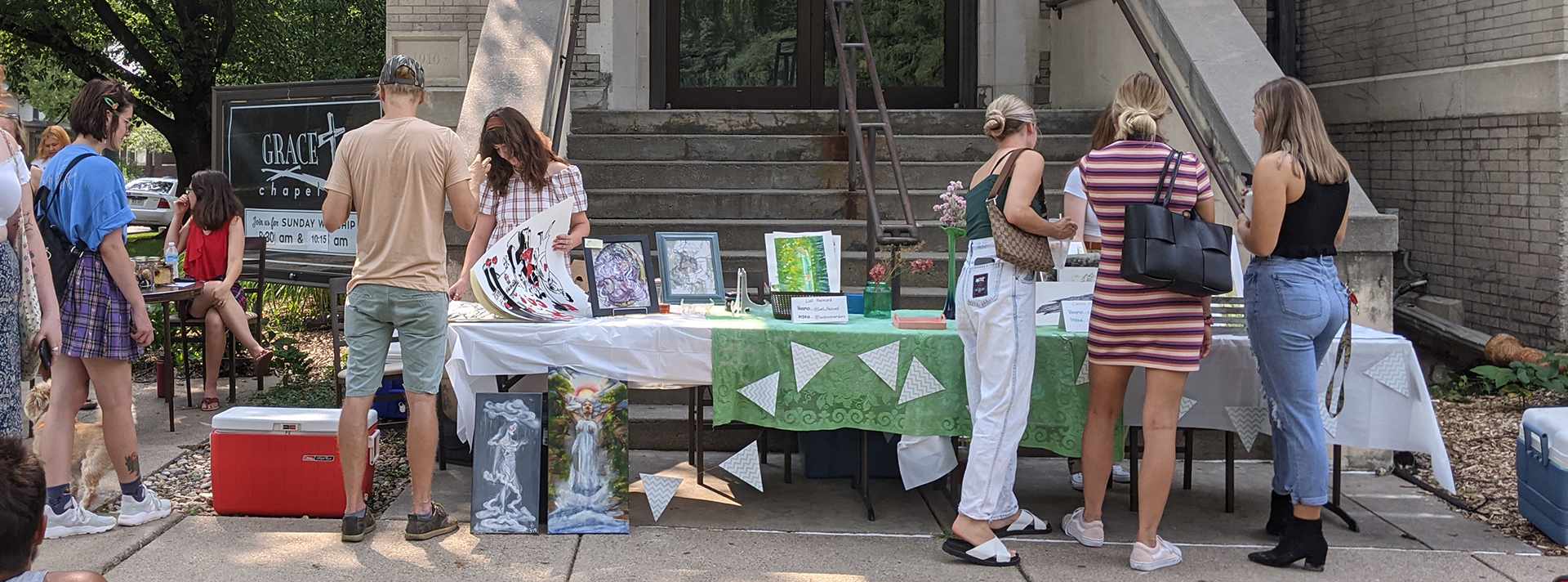 People Gather At A Table Full Of Art Outside