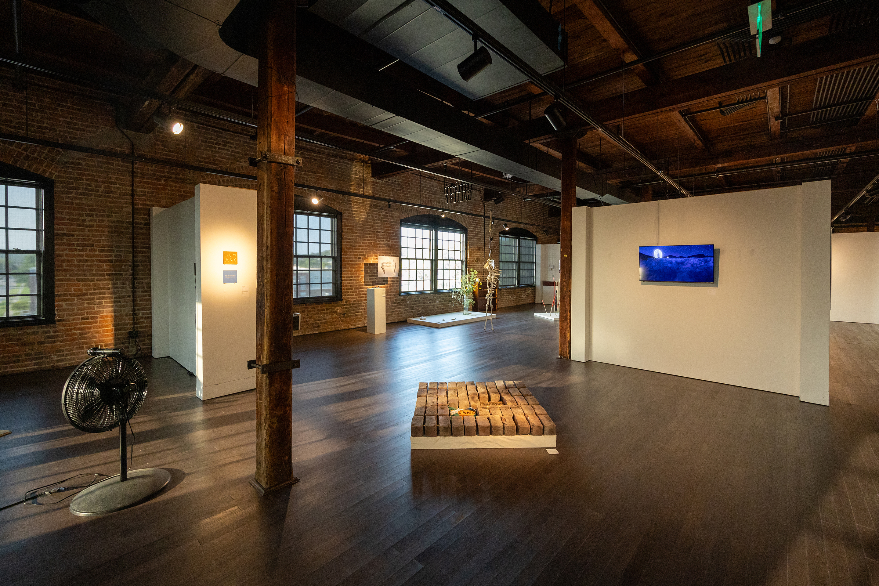 Wide shot of Fortuna group exhibition featuring an instalation of bricks on the floor and flat screen on the wall in the background Photo by Joey Carter