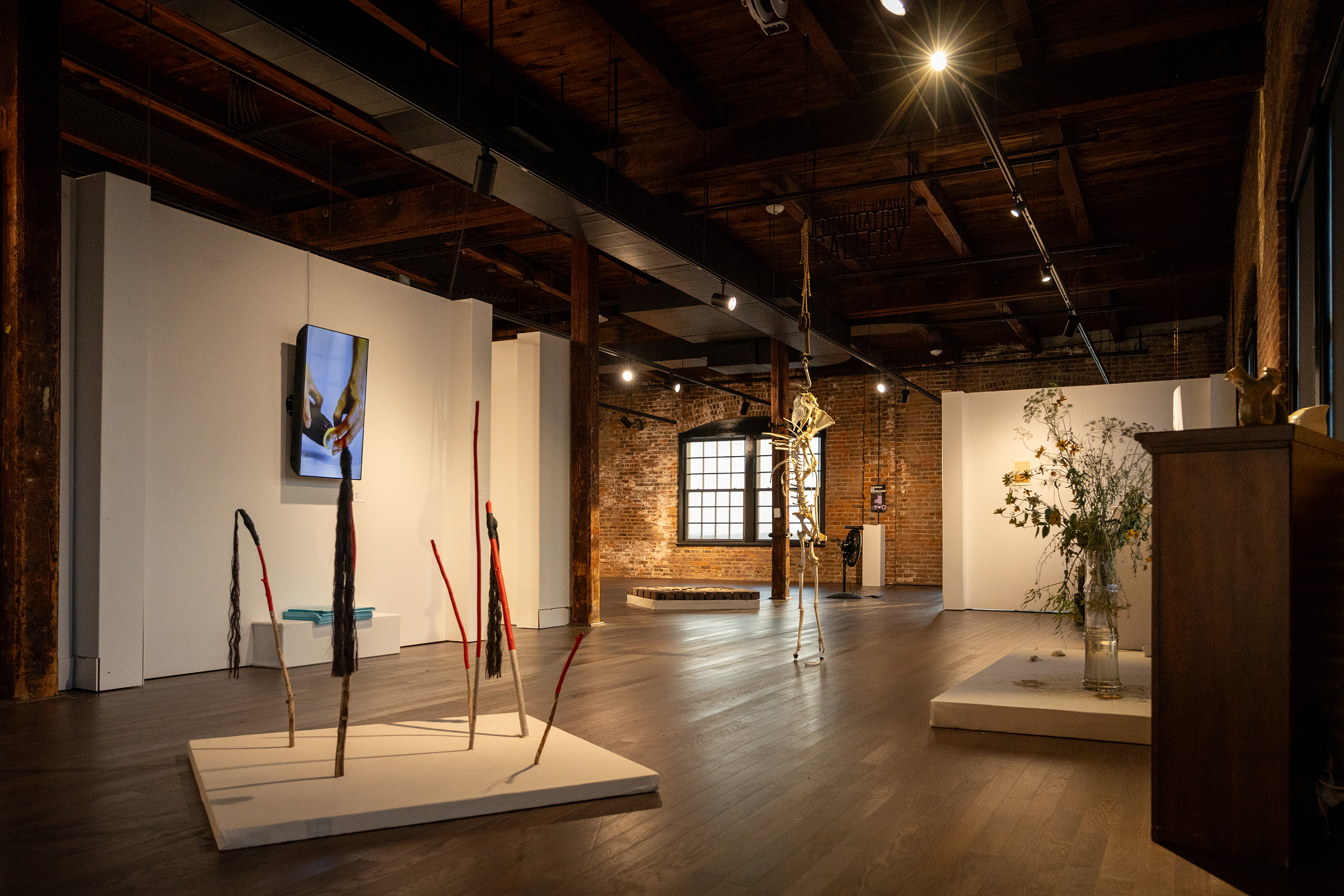 Wide shot of Fortuna group exhibition featuring an instalation of sticks with fiber wrappings Sculptures and a flat screen on the wall are in the background Photo by Joey Carter