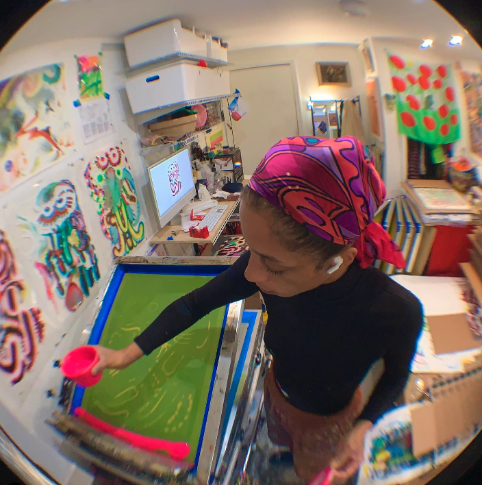 Wide image of Leslie Diuguid pouring ink onto a screen printing screen in her studio the image is from above and is distorted from a wide angle fisheye lens